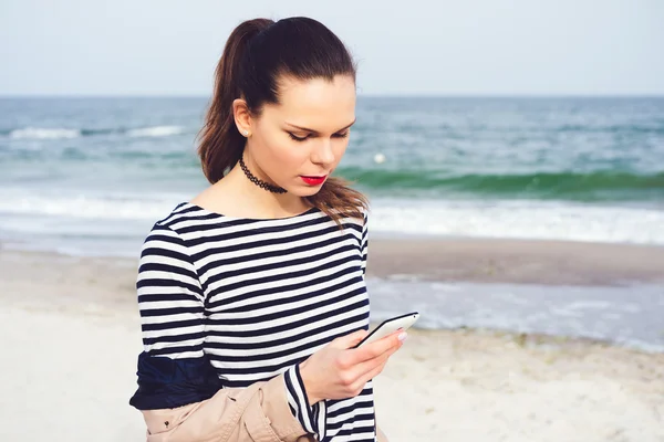 Attractive young woman walking along the beach with a smart phon
