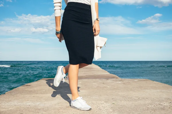 Female legs in a skirt and sneakers on the background of the sea