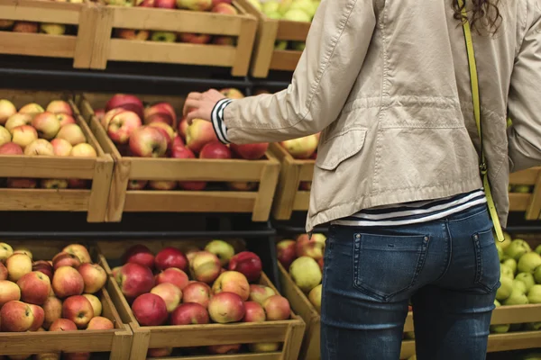 Girl in the beige jacket and blue jeans buys apples