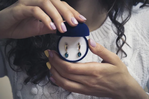 Gold earrings with blue topaz in women's hands