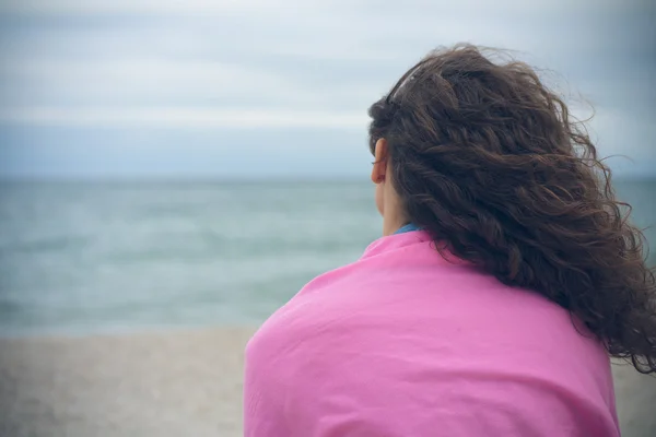 Young woman with curly hair sitting alone on the beach in cloudy