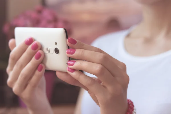 Mobile smart phone in womens hands with a pink manicure