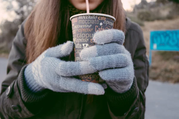 Young woman in knitted gloves drinking coffee from disposable cu