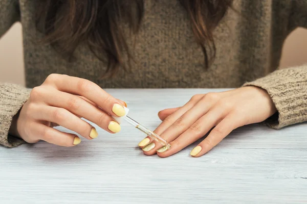 Woman in a brown sweater with yellow manicure applying cosmetic