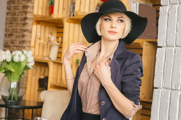 Girl in big black hat with a brim adjusts her blouse