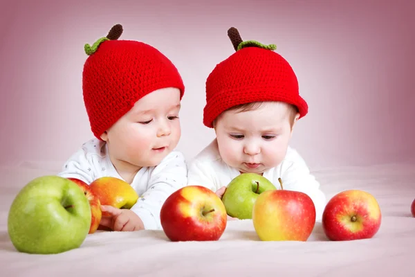 Two cute babies lying in hats on soft blanket with apples