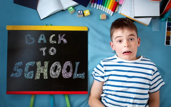 Child lying on blue blanket with blackboard and school accessories