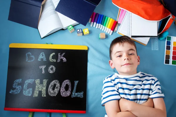 Child lying on blue blanket with blackboard and school accessories