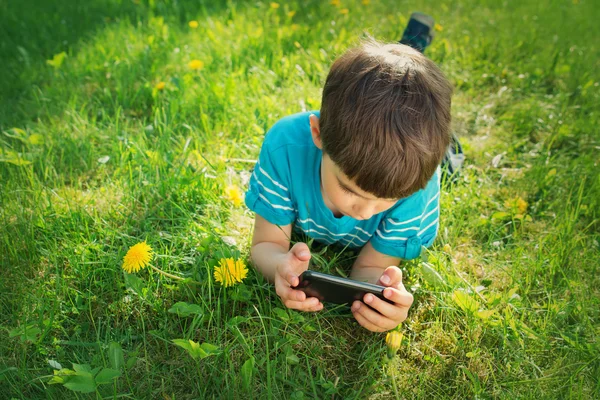 Child lying on the grass in summer suth mobile phone