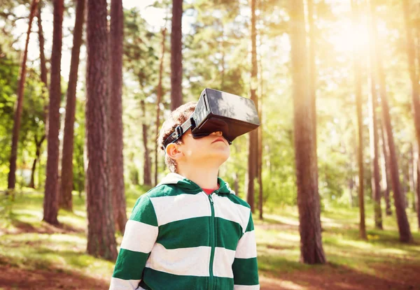Child standing in the forest in virtual reality glasses