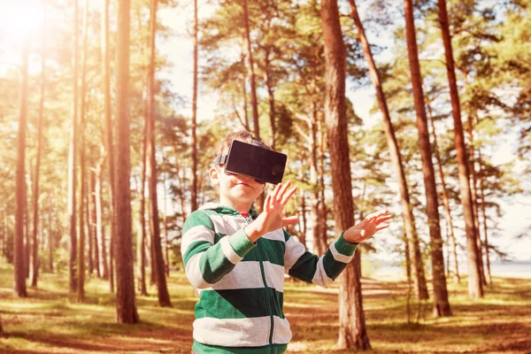 Child standing in the forest in virtual reality glasses
