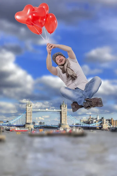 Young man flying on balloons with Tower bridge, London in background