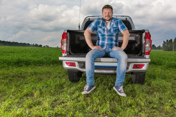 Solid man sitting on car trunk on natural background