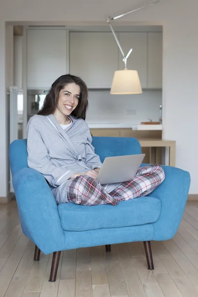 Smiling woman in living room sitting on sofa using laptop. Morning scene women smiling