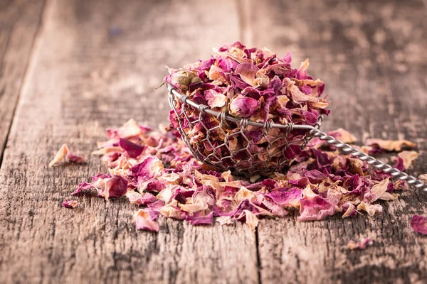 Rose petals and dried flowers in spoon on old wooden table
