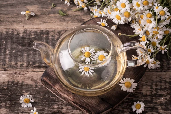 Herbal chamomile tea on a wooden table. Chamomile tea in a transparent cup and camomile flowers on wooden table. Herbal tea for baby\'s stomach. Copy space.