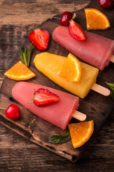 Refreshing fruit popsicle lollies on wooden table with berries and fruits