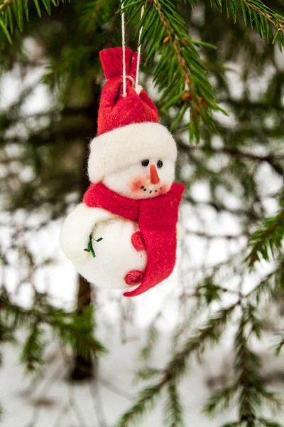 Toy snowman hanging on a snow-covered tree