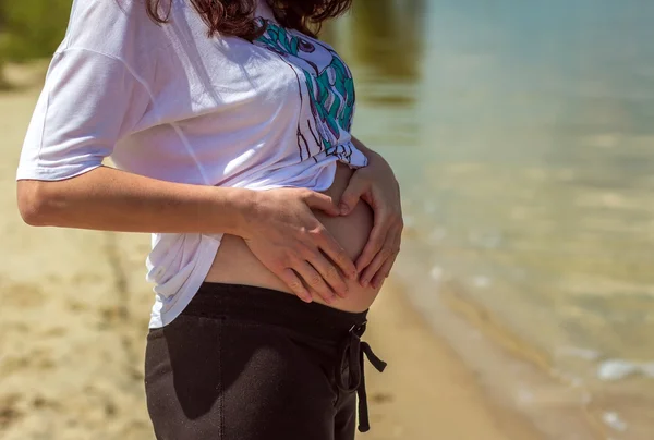 Pregnant woman touches her belly hands making a heart
