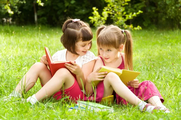 Two little girls reading a book on the nature and talking