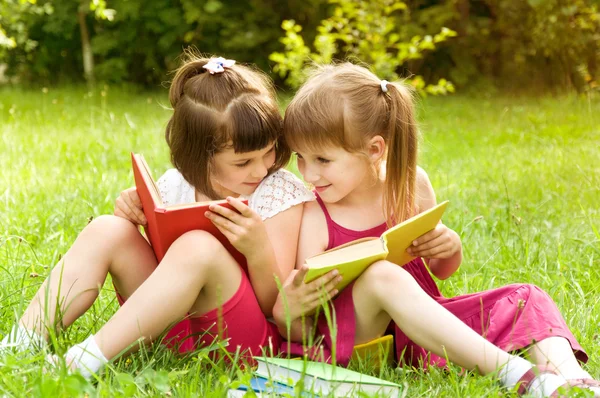 Two little girls reading a book on the nature and talking