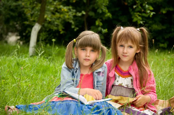 Two little girls reading a book on the nature and talking