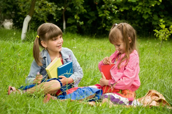 Two little girls reading a book on the nature and talking