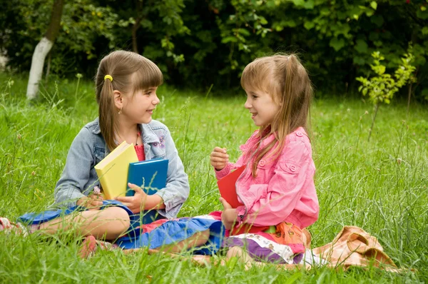 Two little girls reading a book on the nature and talking