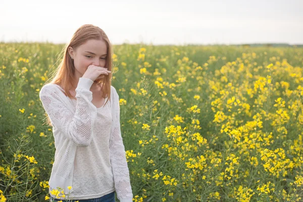 Pollen allergy, girl sneezing in a rapeseed field of flowers