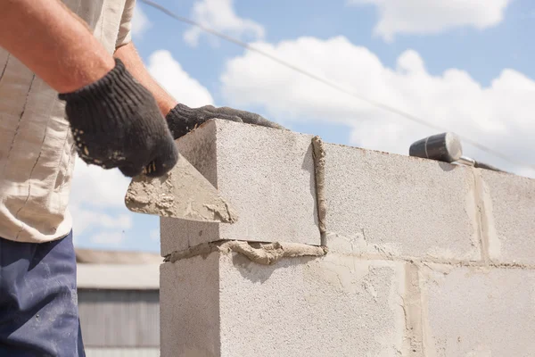 Worker aligns with a spatula, lay brick cinder blocks