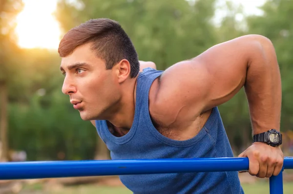 Fitness, sport, exercising, training and lifestyle concept - young man doing triceps dip on parallel bars outdoors