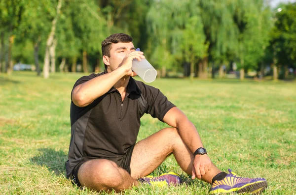 Young muscular man with sport water bottle on sky background.