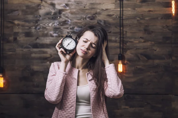 Beautiful young woman with alarm clock in hand and a sour face t