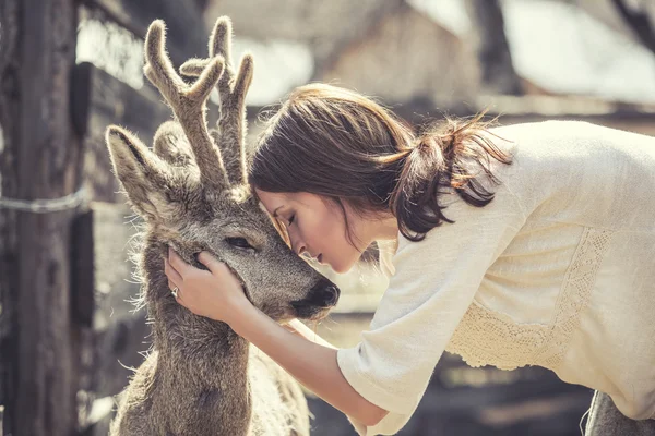 Young beautiful woman hugging animal ROE deer in the sunshine