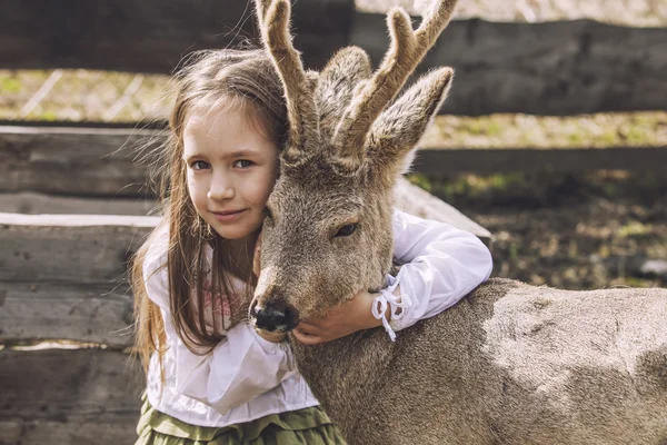 Beautiful little girl hugging animal ROE deer in the sunshine