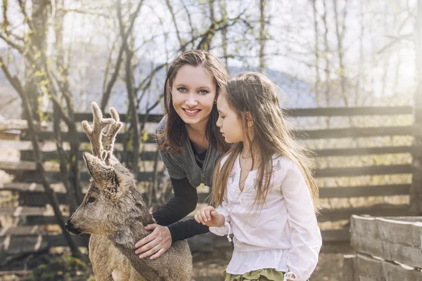 Beautiful little girl and her mom hugging animal ROE deer in the