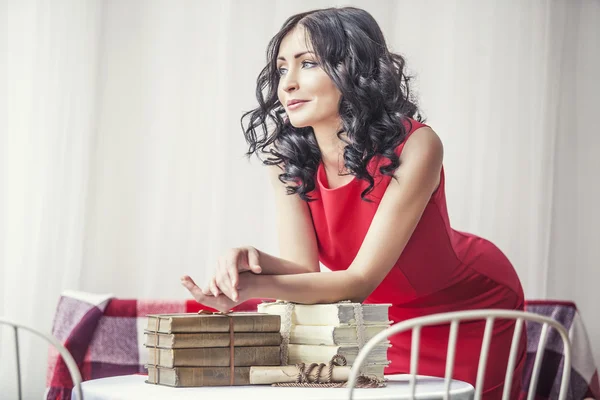 Young beautiful girl in red dress with books on the table