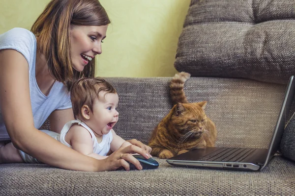 Woman with a baby and a cat at the laptop lying on the couch