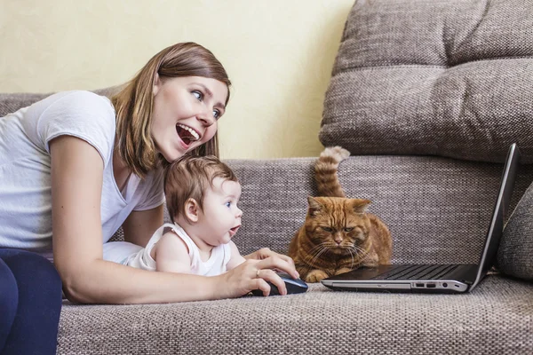 The woman with a baby and a cat at the laptop on the couch