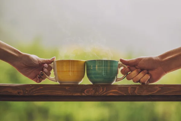 Hands holding mug with hot beverage, with tea on a wooden stand