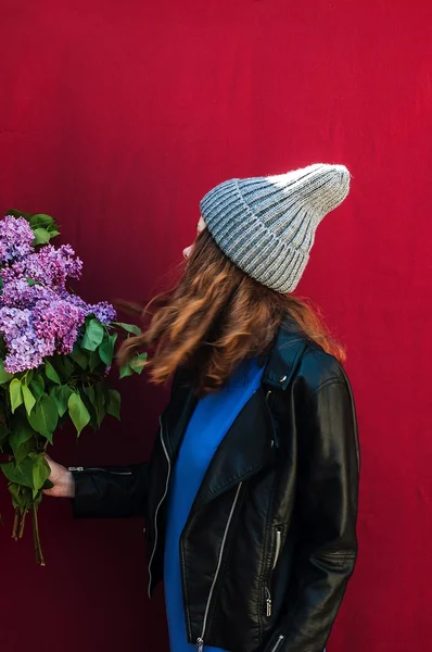 Girl in hat and leather jacket with lilac flowers