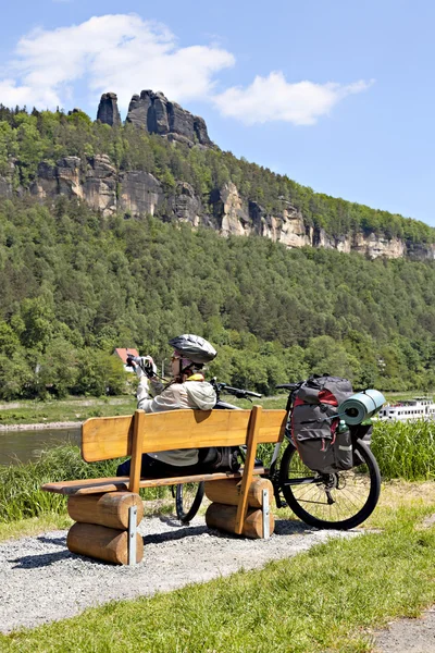 Woman cyclist traveler sitting on the bench and making photo of