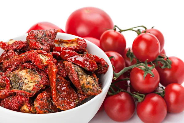 Sun dried tomatoes in white bowl and heap of ripe fresh tomatoes