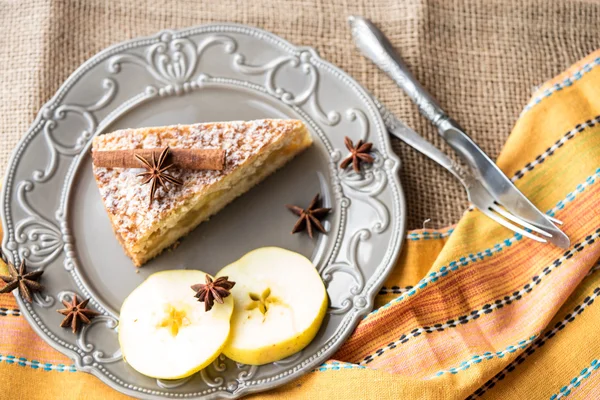 Apple cake decorated with cinnamon stick and star anise on a rustic plate with apple slices