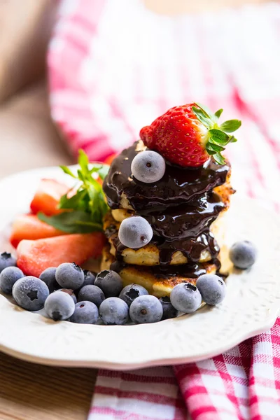 Pancakes with melted chocolate, strawberries and blueberries on a white plate