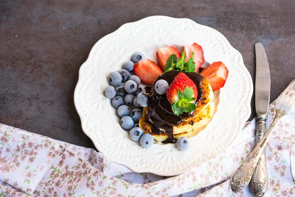 Pancakes with melted chocolate, strawberries and blueberries on a white plate