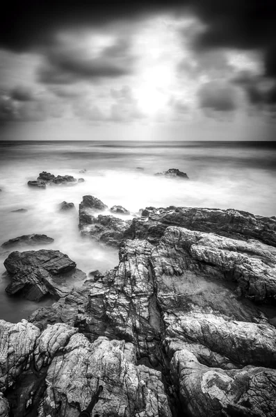 Black and white image soft wave hitting the rock along the coastline.