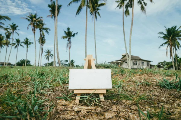 Business success concept. white canvas frame on wooden easel over blur village  background and green grass.