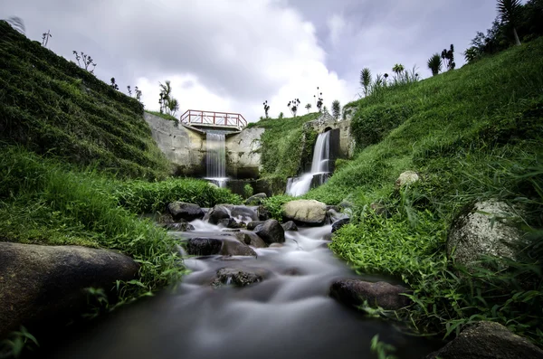 Beautiful scenery of hidden waterfall with cloudy sky in the middle of tea farm at Cameron Highland, Malaysia.Soft focus and some motion blur due to long exposure. Focus in the center