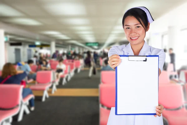The blank board held by asian nurse with terminal seat at airport in background , medical tourism concept